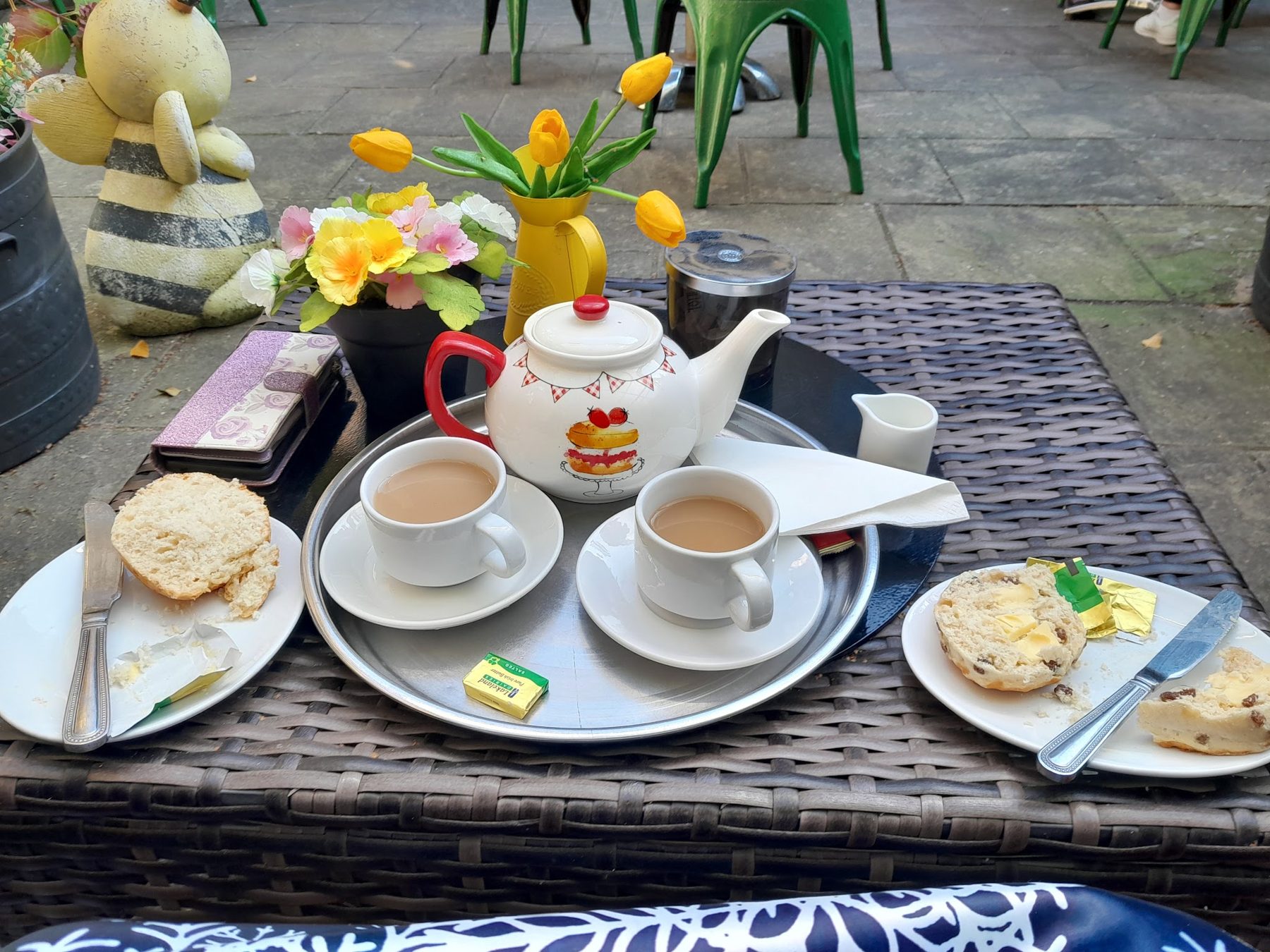 Tea for two with a teapot, scones and daffodils on an outdoor table